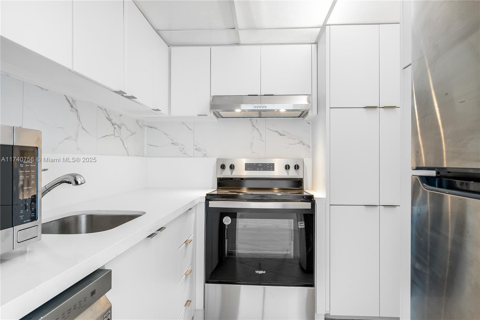 A modern kitchen features white cabinets, stainless steel appliances, and a marble-patterned backsplash — 1000 West Ave # 1008, Miami Beach FL 33139, MIAMI BEACH, FL