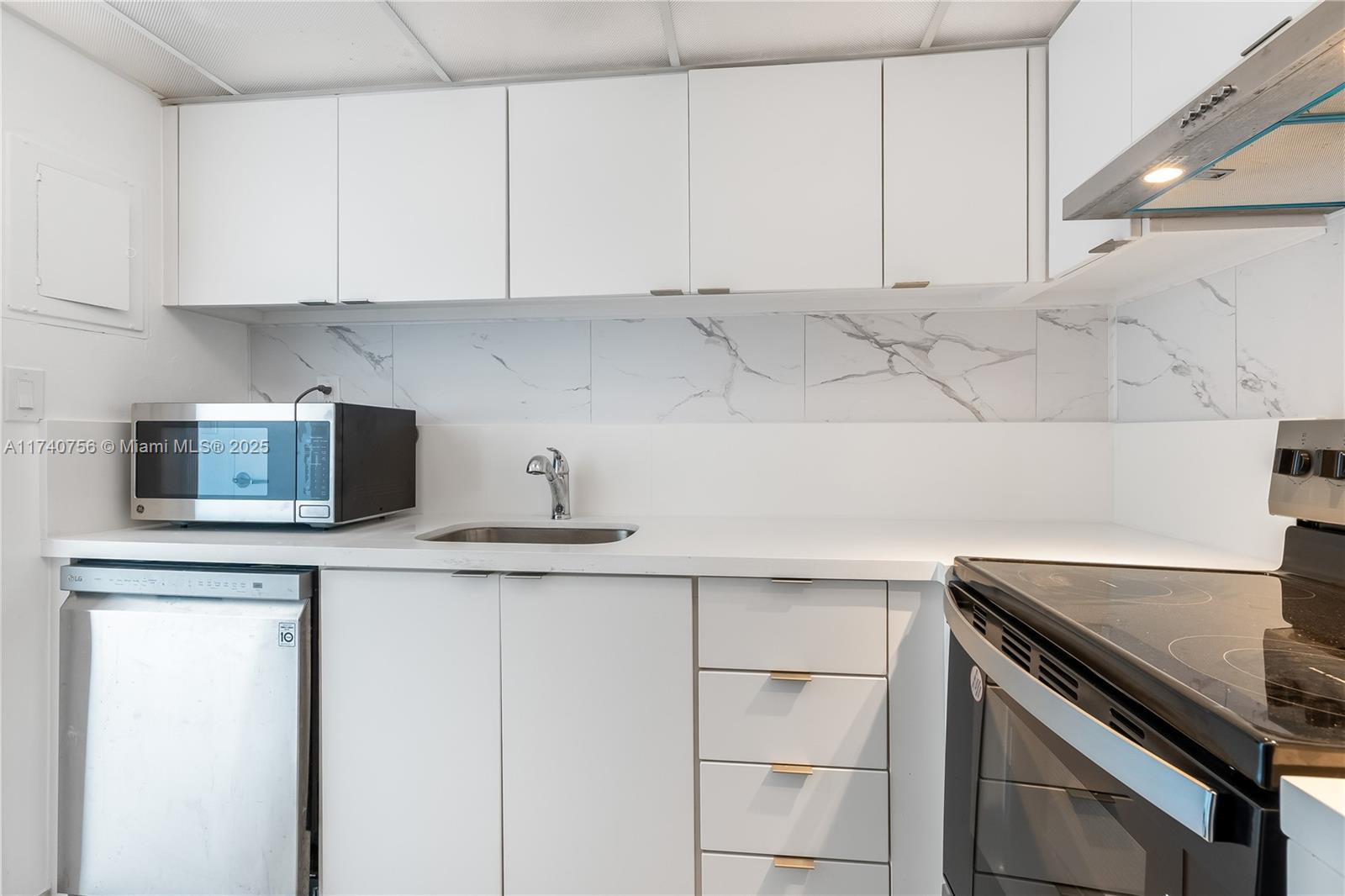 A kitchen features white cabinets, a stainless steel dishwasher, a microwave, and marble-patterned backsplash tiles — 1000 West Ave # 1008, Miami Beach FL 33139, MIAMI BEACH, FL