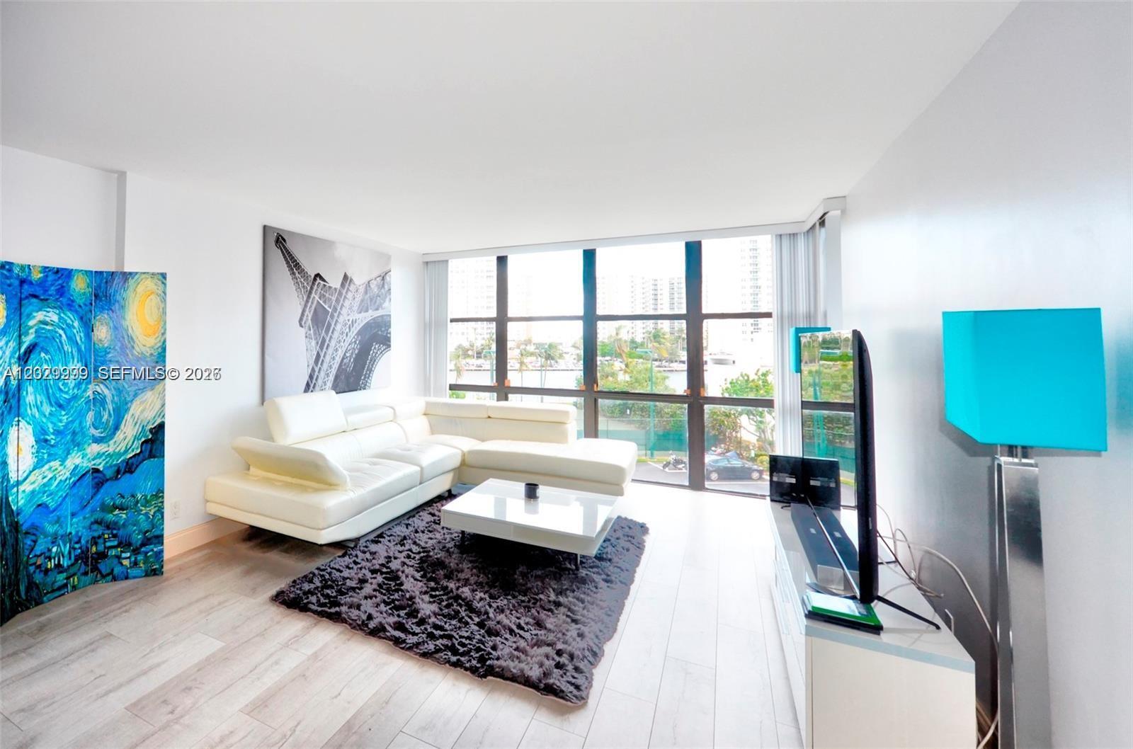 A living room features a white sectional sofa, a dark rug, and floor-to-ceiling windows — 1000 Parkview Dr # 426, Hallandale Beach FL 33009, HALLANDALE BEACH, FL