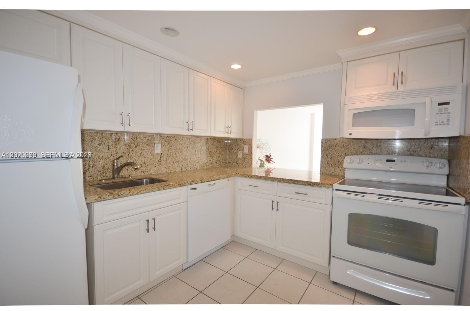 A kitchen features white cabinets, granite countertops, white appliances, and light-colored tile flooring — 1000 Parkview Dr # 426, Hallandale Beach FL 33009, HALLANDALE BEACH, FL