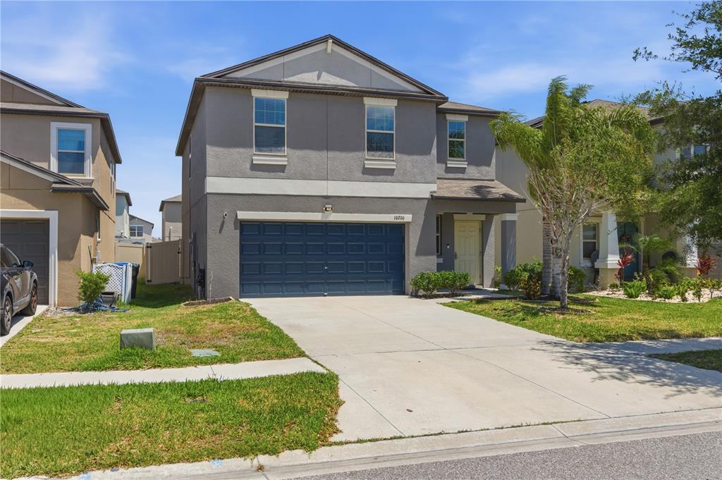A two-story suburban house with a gray stucco exterior and a blue two-car garage — 10206 COOL WATERLILY AVENUE, RIVERVIEW, FL