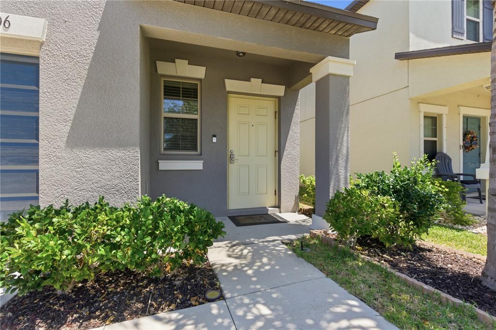 A concrete walkway leads to the front entrance of a house with a beige door — 10206 COOL WATERLILY AVENUE, RIVERVIEW, FL