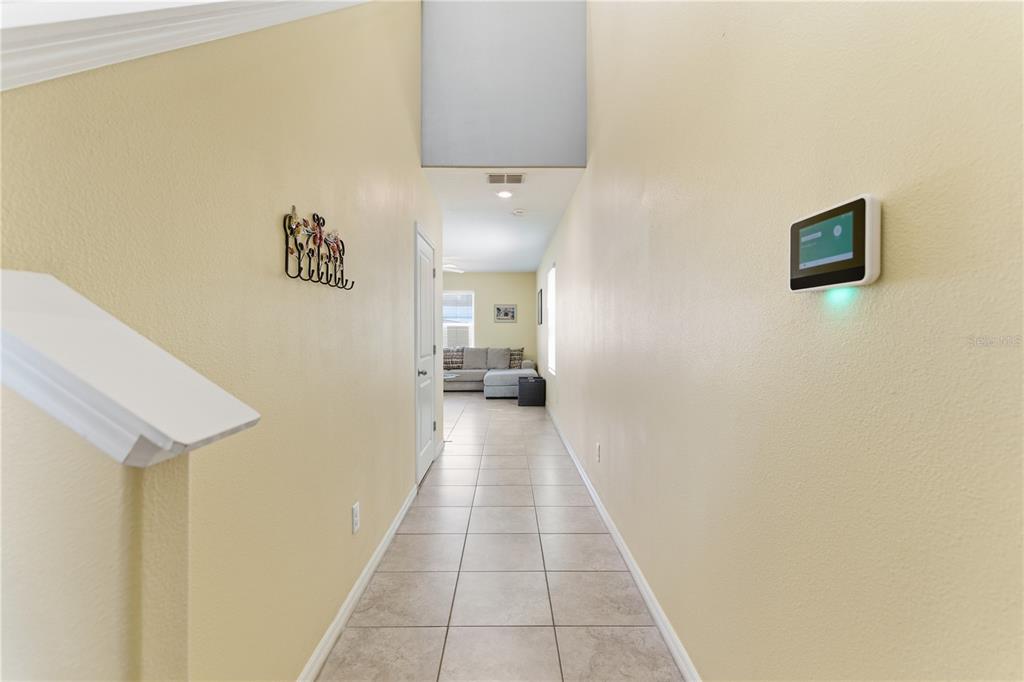 A tiled hallway leads from a staircase toward a living room with a gray sofa — 10206 COOL WATERLILY AVENUE, RIVERVIEW, FL