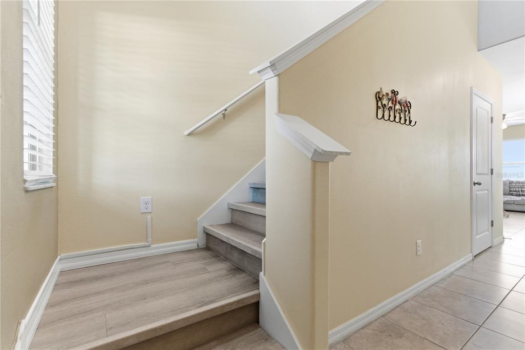 A staircase with light wood-look flooring leads upward next to a beige wall — 10206 COOL WATERLILY AVENUE, RIVERVIEW, FL