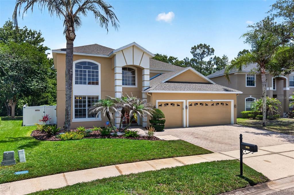 A two-story suburban house with a tan stucco exterior, a two-car garage, and palm trees — 1880 OAK GROVE CHASE DRIVE, ORLANDO, FL