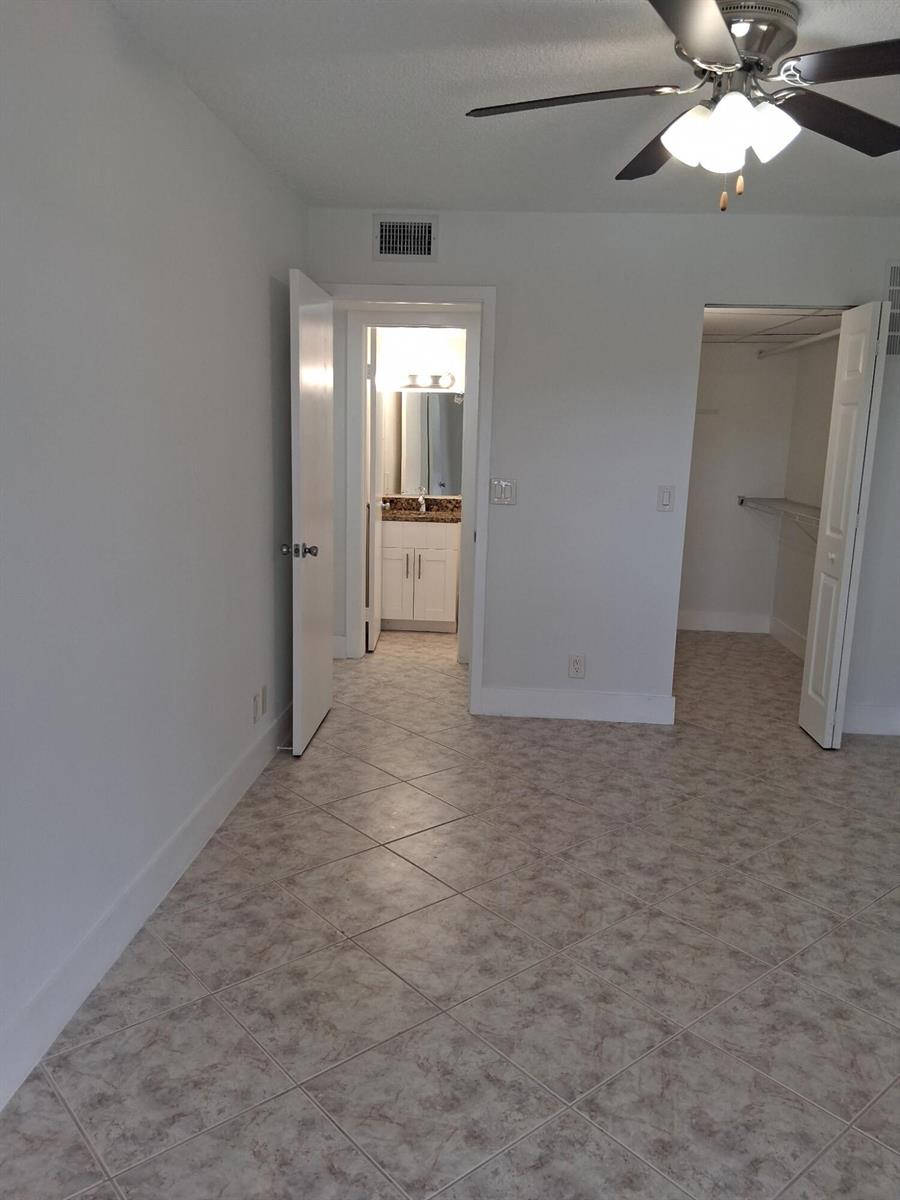 A bedroom with tile flooring, a ceiling fan, an open closet, and an attached bathroom — 2100 Springdale Boulevard # 303, Palm Springs FL 33461, PALM SPRINGS, FL