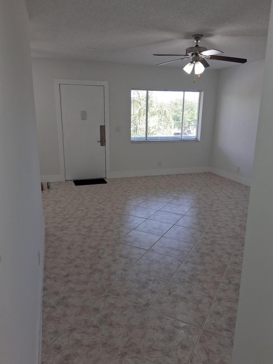 An empty room features light-colored tile flooring, a ceiling fan, and a white entry door — 2100 Springdale Boulevard # 303, Palm Springs FL 33461, PALM SPRINGS, FL
