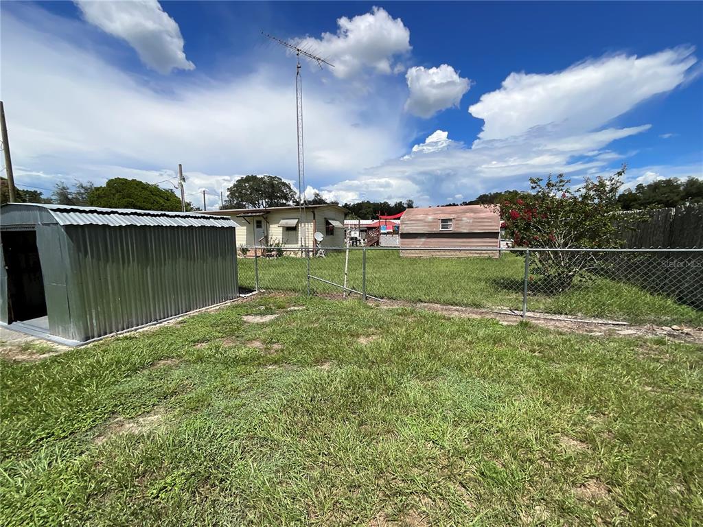 A metal shed sits in a grassy backyard enclosed by a chain-link fence — 9624 SE 163RD LANE, SUMMERFIELD, FL