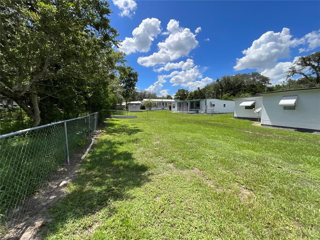 A grassy backyard features a chain-link fence, mature trees, and several mobile homes — 9624 SE 163RD LANE, SUMMERFIELD, FL