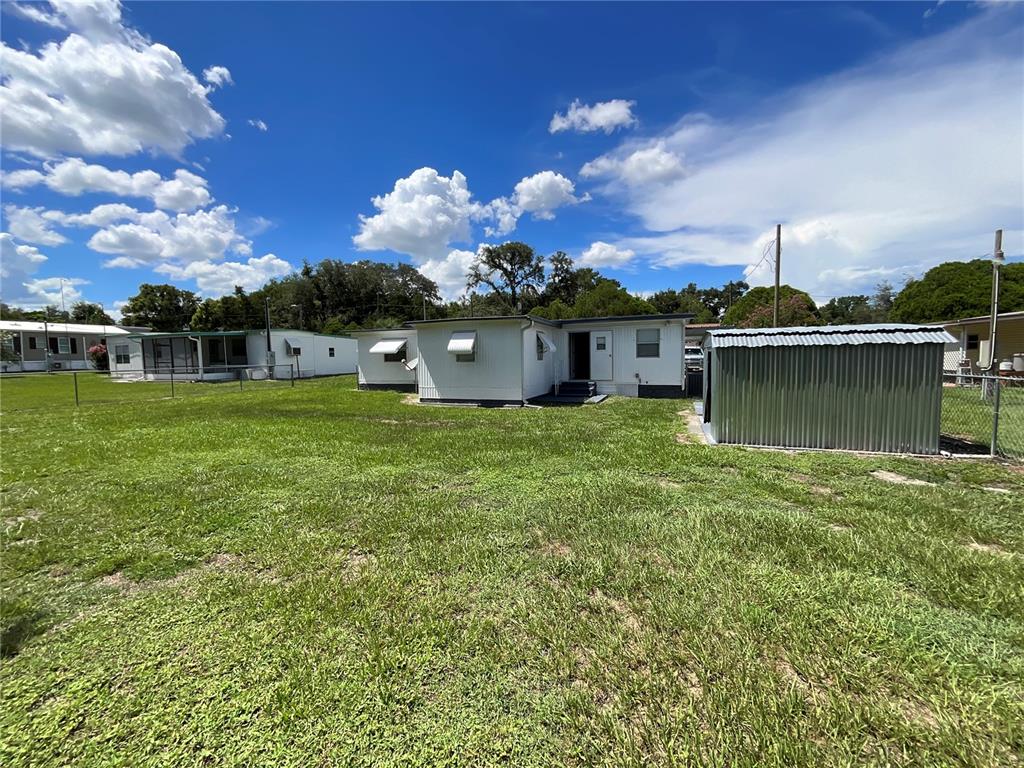 A white mobile home with a metal shed sits on a grassy lot under blue skies — 9624 SE 163RD LANE, SUMMERFIELD, FL