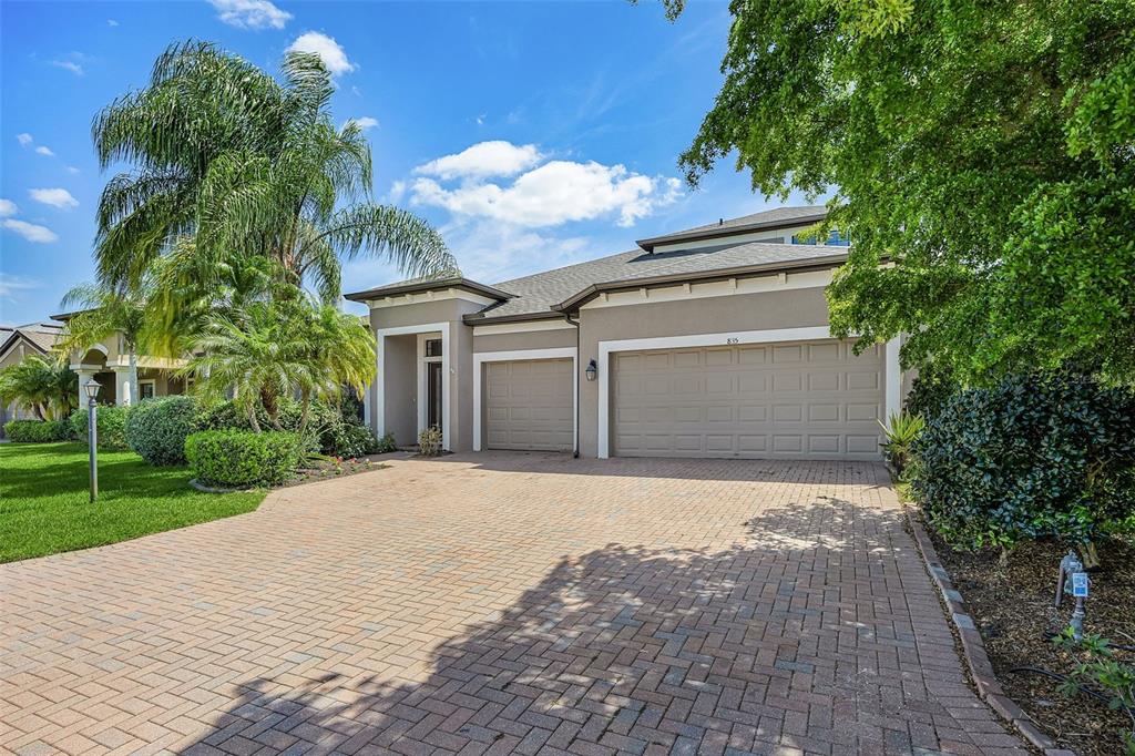 A tan house with a three-car garage and a paved driveway under a blue sky — 835 129TH STREET NE, BRADENTON, FL