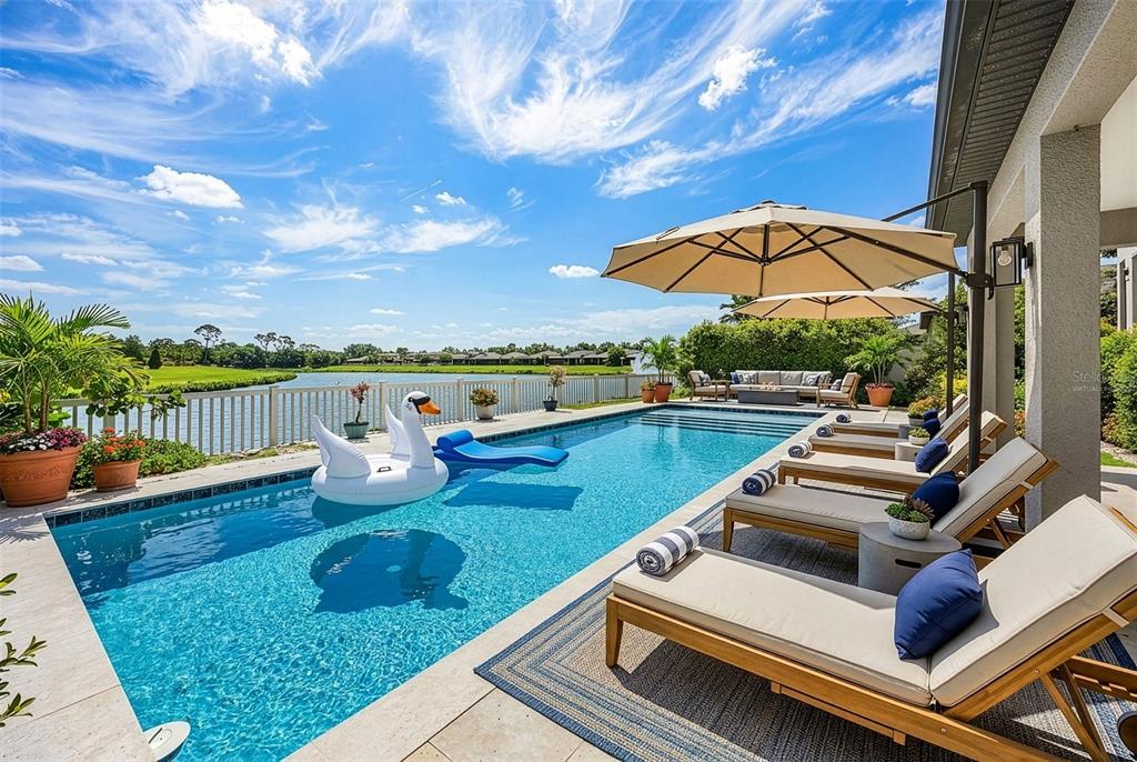 A swimming pool with lounge chairs and a swan float overlooks a lake and lawn — 835 129TH STREET NE, BRADENTON, FL