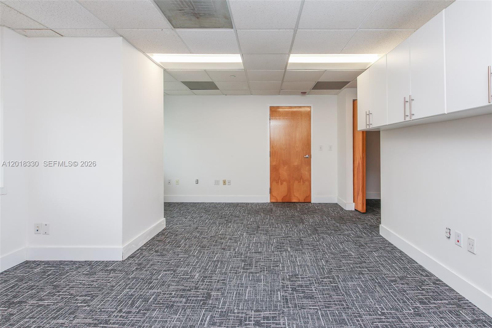 An office space features white walls, gray patterned carpet, drop ceilings, and wooden doors — CORAL SPRINGS, FL