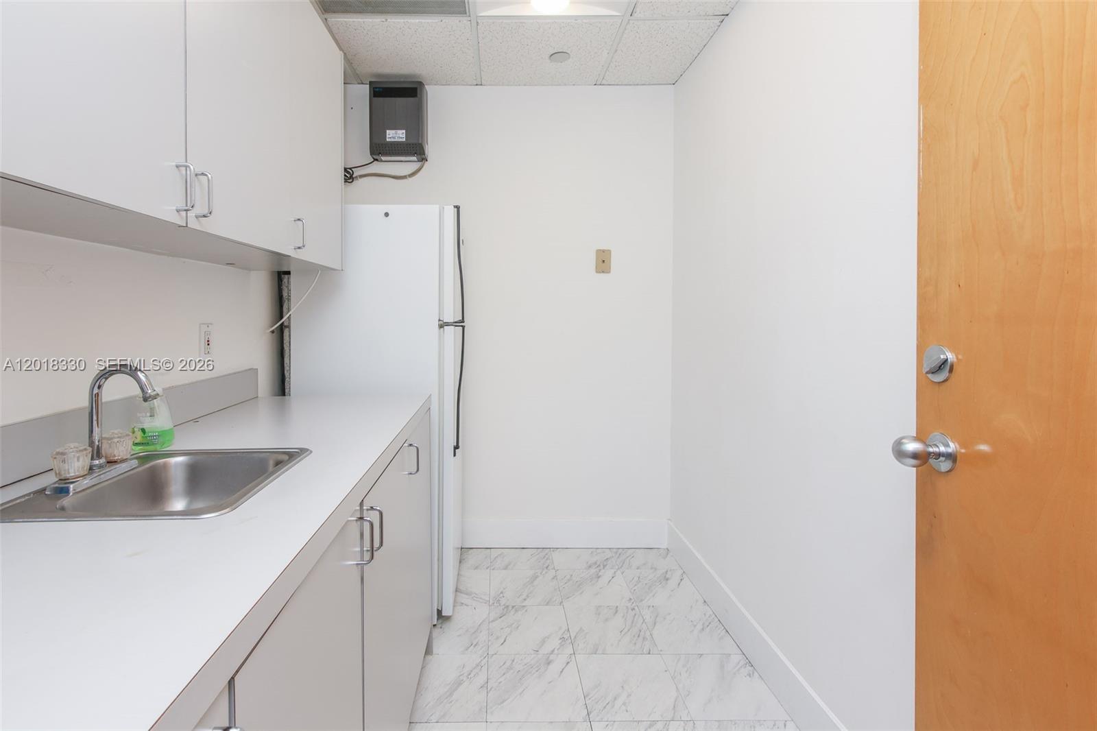 A small kitchenette features white cabinets, a stainless steel sink, and a white refrigerator — CORAL SPRINGS, FL