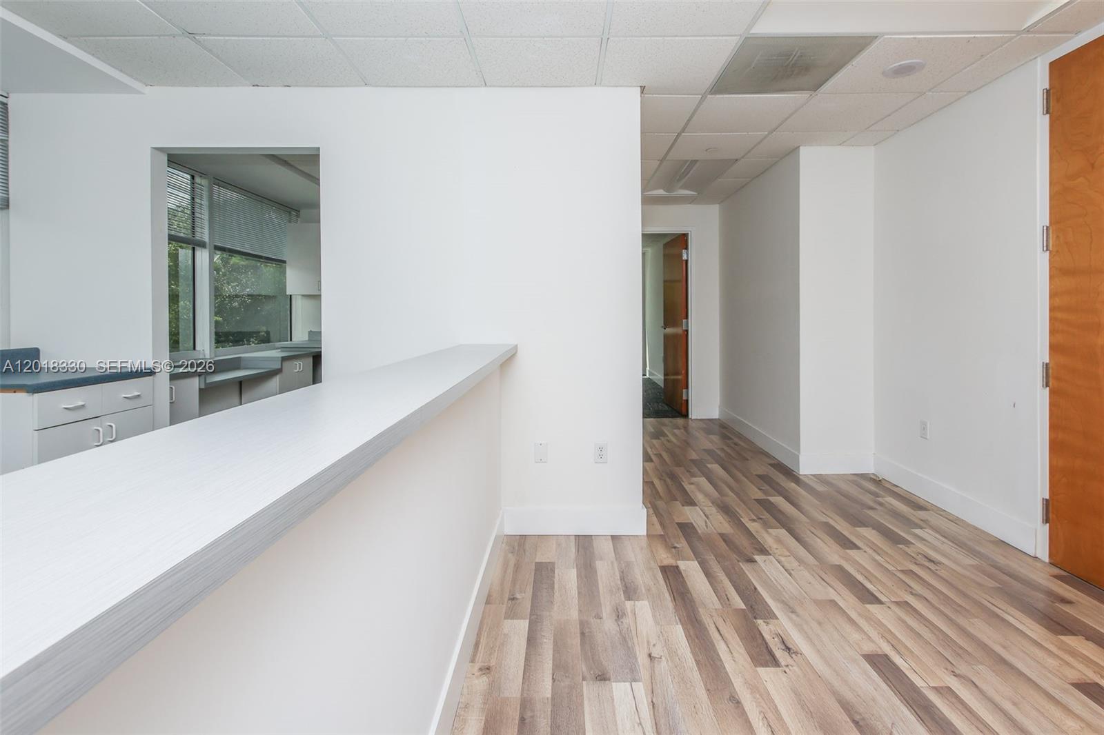 A bright office space features a white reception counter, wood-look flooring, and a drop ceiling — CORAL SPRINGS, FL