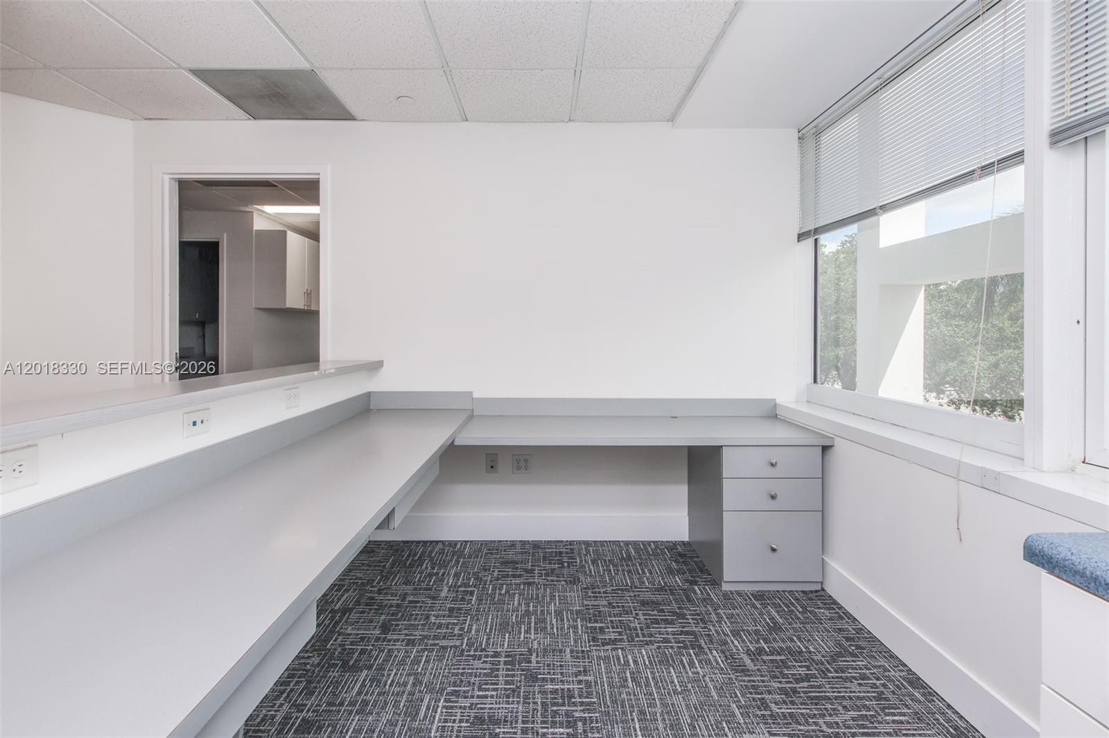 An office space features a gray L-shaped desk, gray carpet, and a large window — CORAL SPRINGS, FL