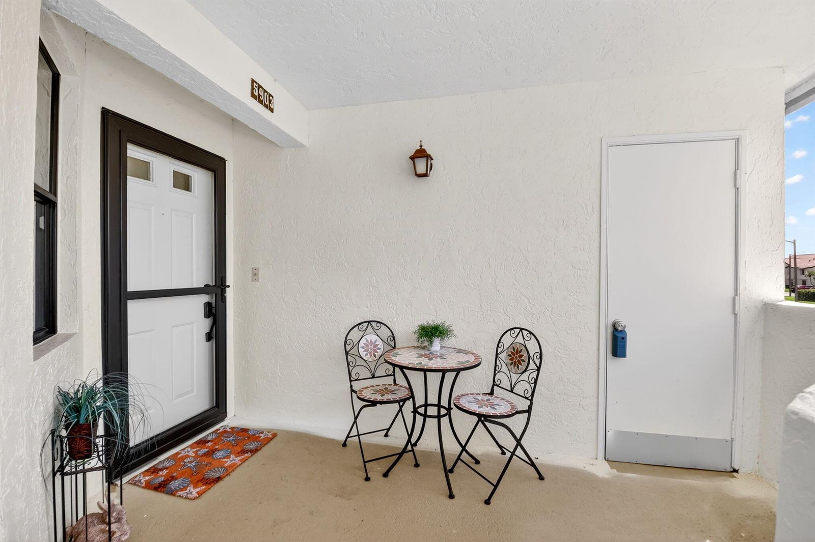A covered patio features a small mosaic bistro set, a white door, and a screen door — 5903 Parkwalk Drive # 623, Boynton Beach FL 33472, BOYNTON BEACH, FL