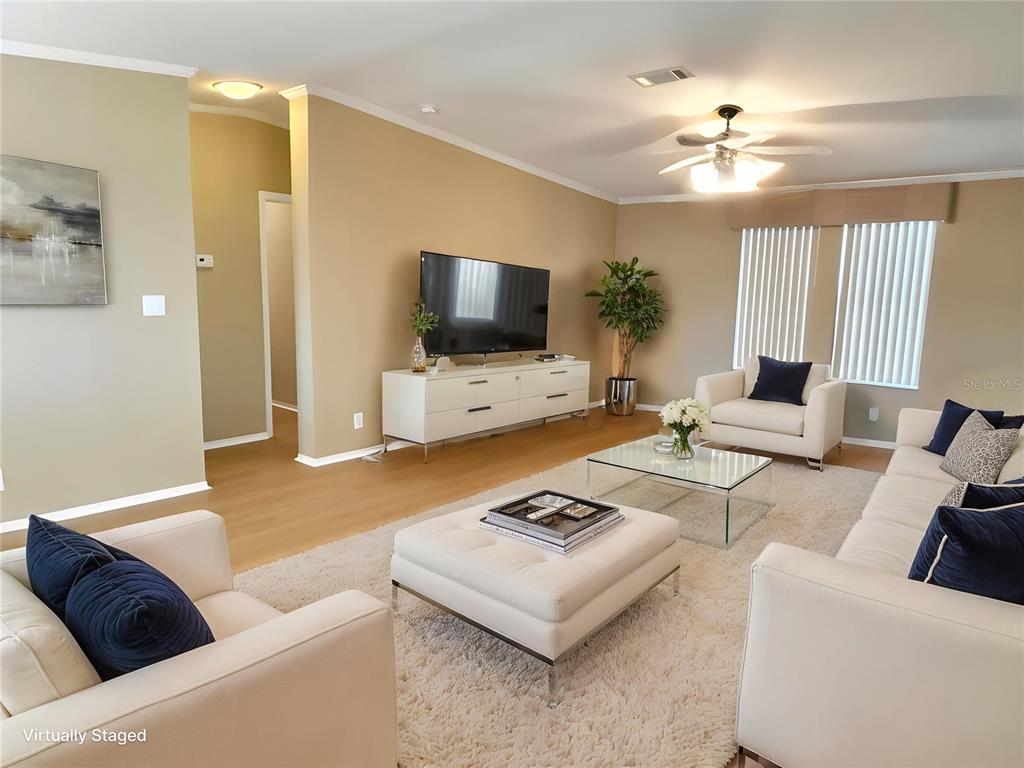 A living room with beige walls, light wood floors, white furniture, and a large television — 6817 MOUNT PLEASANT ROAD NE UNIT 49, ST PETERSBURG, FL