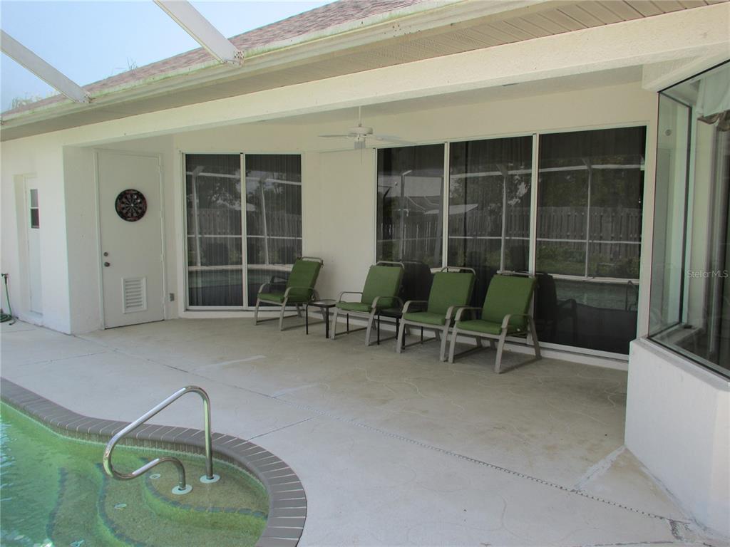 A covered patio features a concrete floor, four green chairs, and a swimming pool — 23404 PEACHLAND BOULEVARD, PORT CHARLOTTE, FL