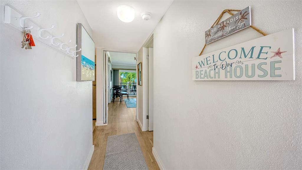 A hallway features light wood flooring, wall-mounted decor, and a view into a living area — 2850 GULF OF MEXICO DRIVE UNIT 4, LONGBOAT KEY, FL