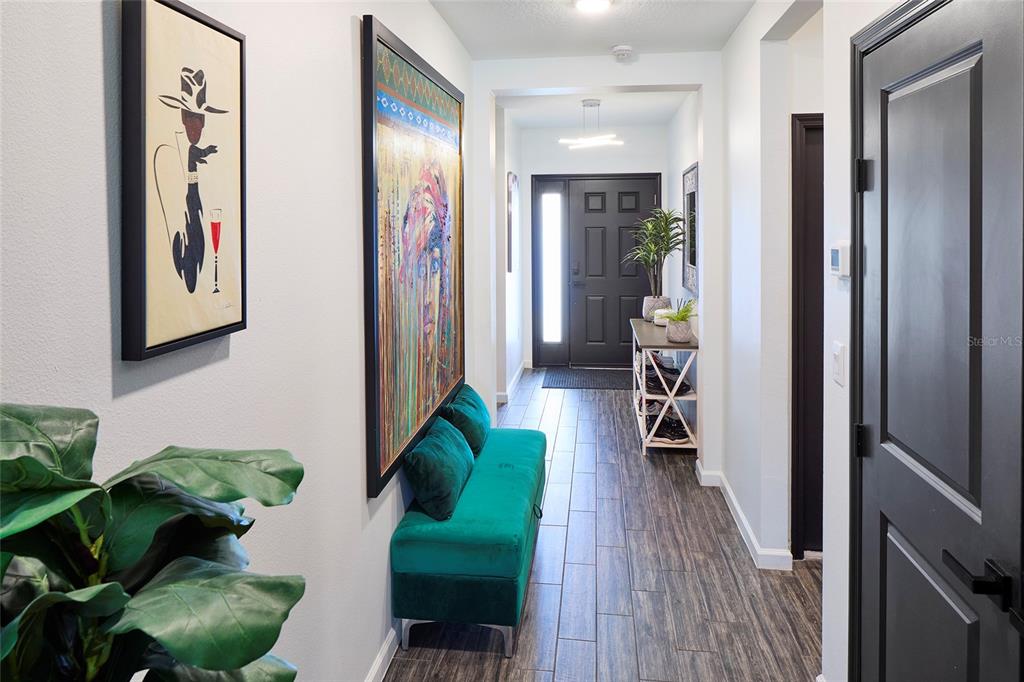A hallway features wood-look tile flooring, a teal velvet bench, and two large framed artworks — 832 CAMBRIDGE DRIVE, WINTER HAVEN, FL