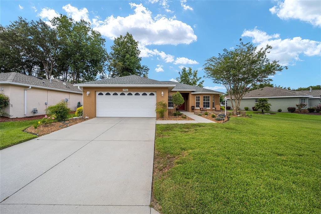 A single-story house with a white garage door, tan stucco exterior, and a green lawn — 7962 SW 83RD PLACE, OCALA, FL