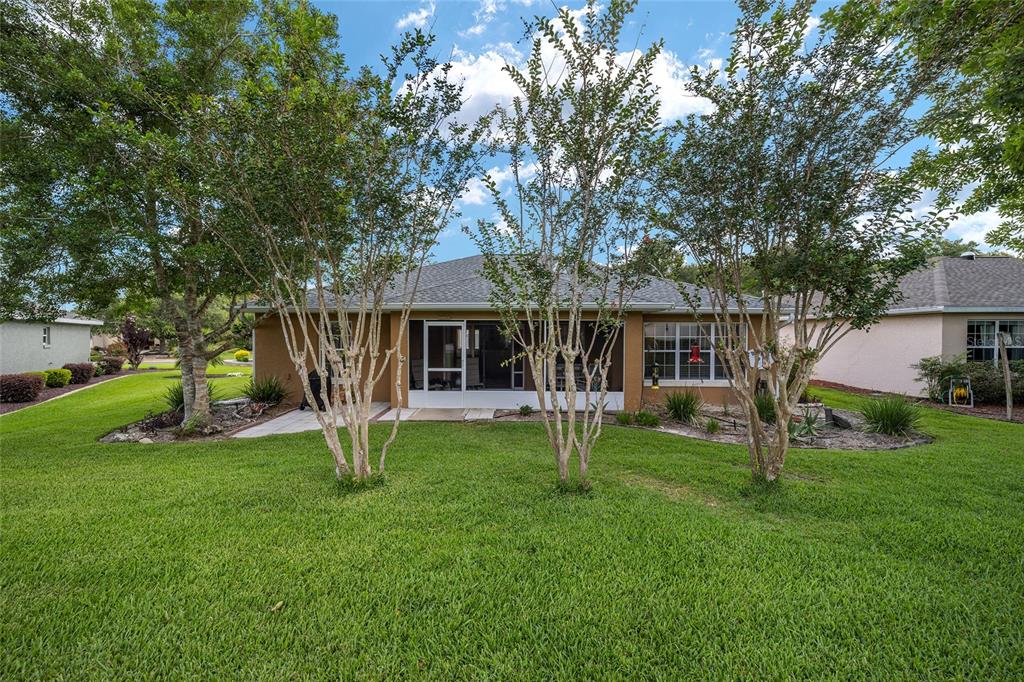 The back exterior of a tan house features a screened-in lanai and mature landscaping — 7962 SW 83RD PLACE, OCALA, FL