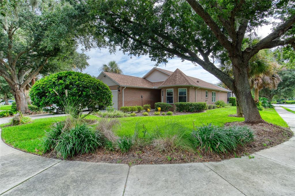 A single-story brick house with a turret-style roof sits behind a landscaped lawn and trees — 38 OLD MACON DRIVE, ORMOND BEACH, FL
