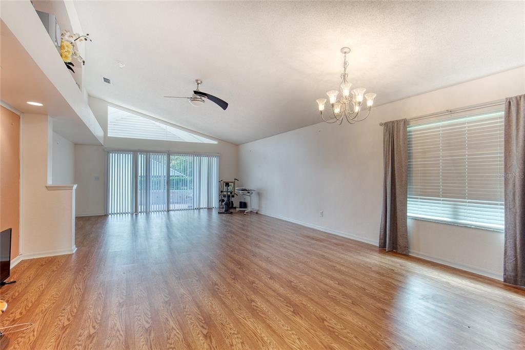 A spacious living room features wood-look flooring, a vaulted ceiling, a chandelier, and sliding doors — 38 OLD MACON DRIVE, ORMOND BEACH, FL