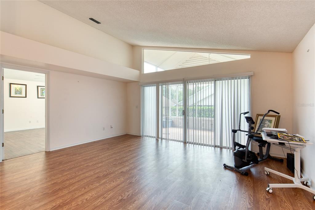 A living room with wood-look flooring, vaulted ceilings, and sliding glass doors leading to a patio — 38 OLD MACON DRIVE, ORMOND BEACH, FL
