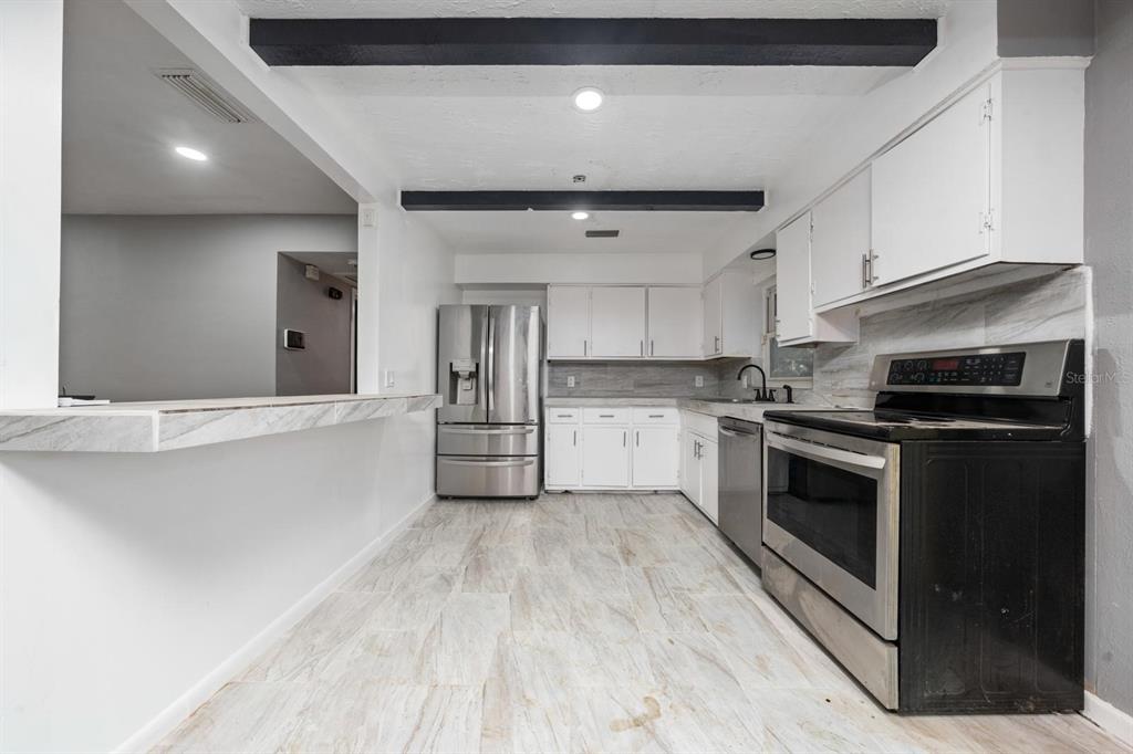 A kitchen features white cabinets, stainless steel appliances, and light-colored tile flooring — 6531 HILL TOP ROAD, ORLANDO, FL