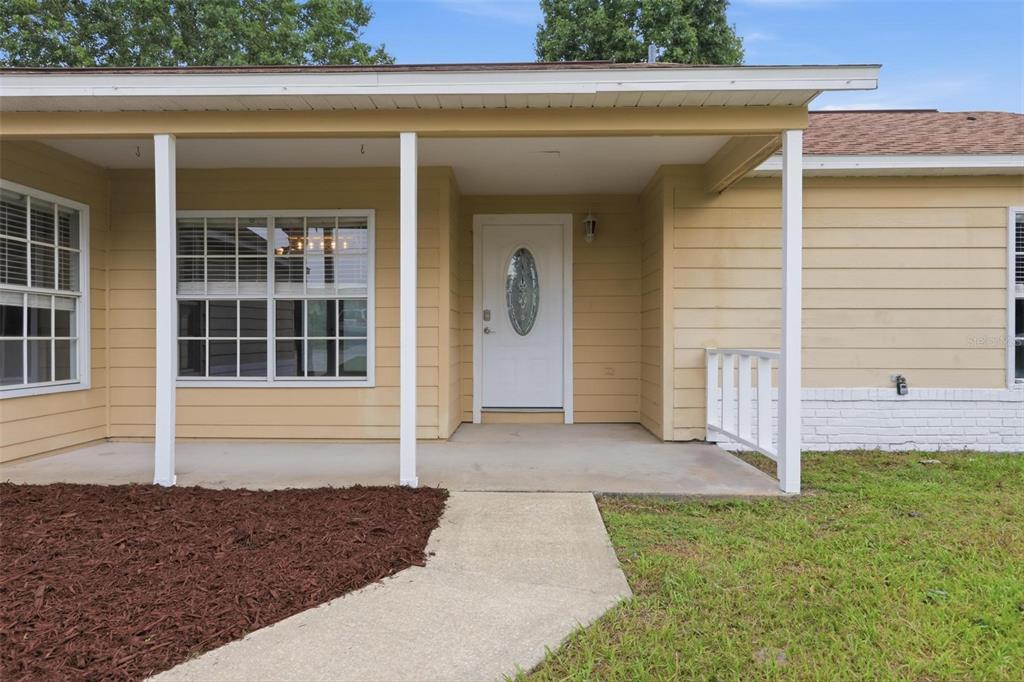 A beige house exterior features a covered front porch, white door, and a concrete walkway — 2695 KEENE LANE, DELTONA, FL