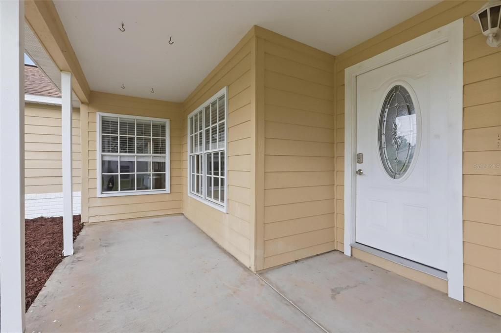 A covered front porch with beige siding, a white front door, and two windows — 2695 KEENE LANE, DELTONA, FL