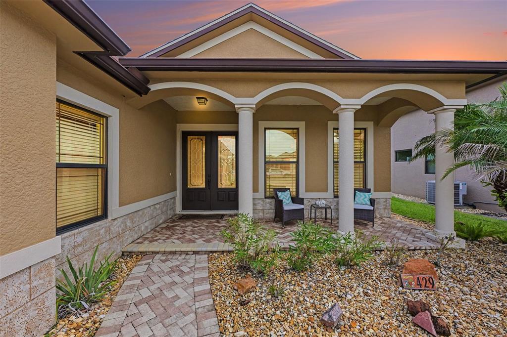 A tan stucco house exterior features a brick-paved walkway, covered porch with columns, and double doors — 429 HARMONY LANE, TITUSVILLE, FL