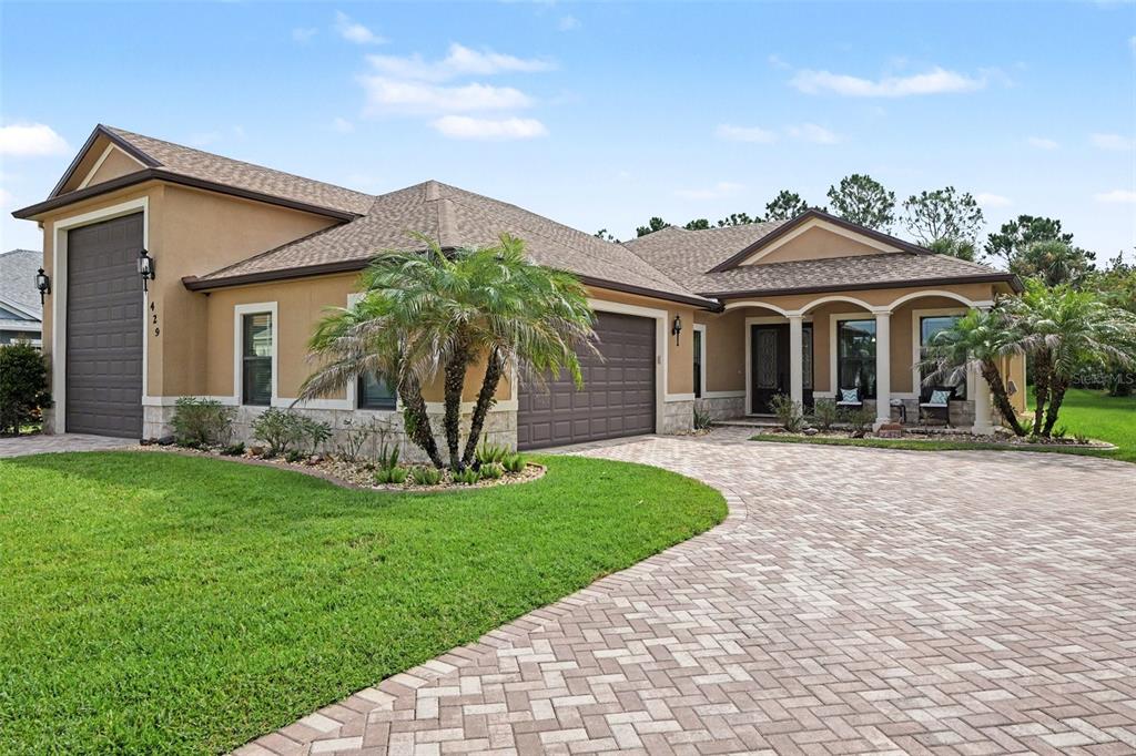 A tan single-story house with a paved driveway, a three-car garage, and a palm tree — 429 HARMONY LANE, TITUSVILLE, FL
