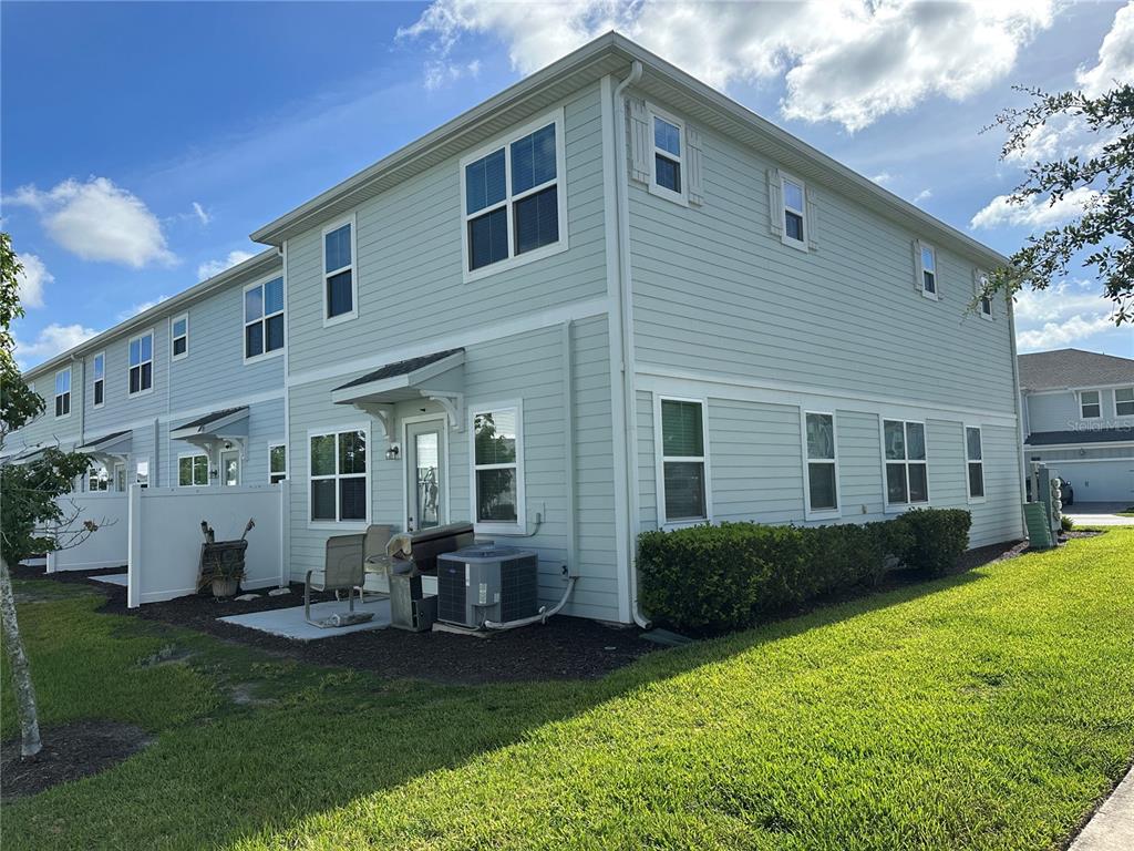 The exterior of a light green two-story townhouse features a small patio and landscaping — 2900 TITLE STREET, KISSIMMEE, FL