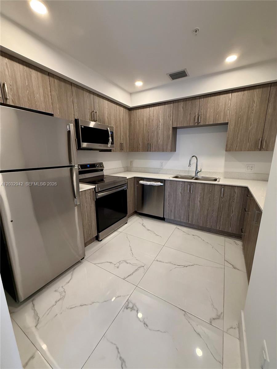 A modern kitchen features stainless steel appliances, wood-grain cabinets, and white marble-patterned tile floors — 11150 NW 82nd St # 409, Doral FL 33178, DORAL, FL