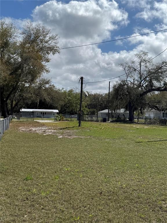 A grassy, vacant residential lot features a utility pole and surrounding trees under a cloudy sky — 1700 ORANGE LANE, KISSIMMEE, FL