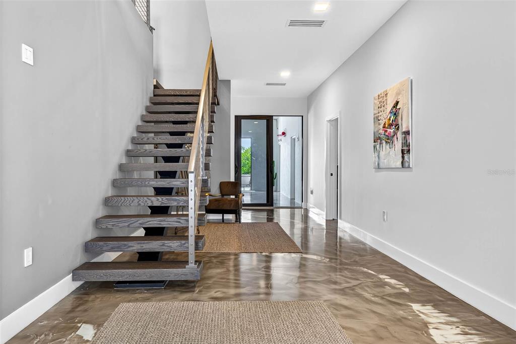A modern entryway features a floating wooden staircase, polished concrete floors, and a glass door — 131 FOREST HILLS DRIVE, REDINGTON SHORES, FL