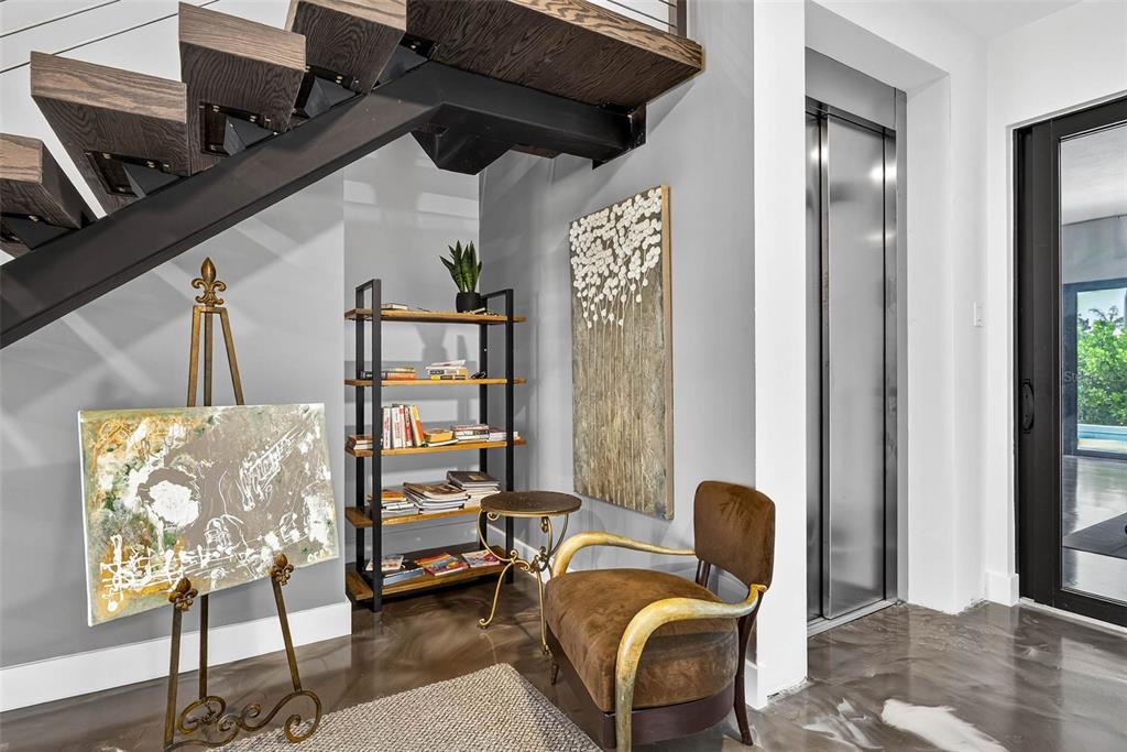 A modern entryway features a floating staircase, a metal elevator, a bookshelf, and an armchair — 131 FOREST HILLS DRIVE, REDINGTON SHORES, FL