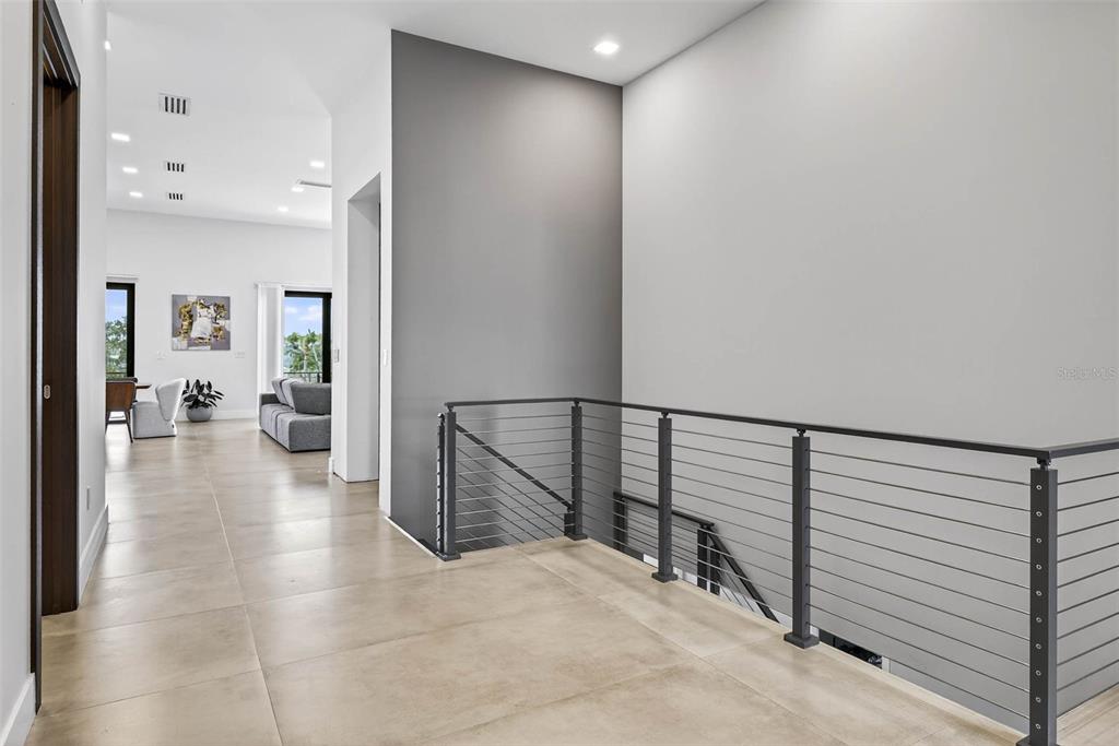 A modern hallway features large beige floor tiles, a cable railing, and a gray accent wall — 131 FOREST HILLS DRIVE, REDINGTON SHORES, FL