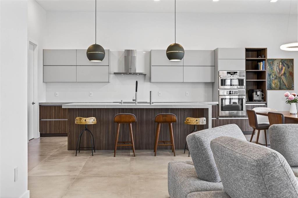 A modern kitchen features a large wood-paneled island, grey cabinetry, and two spherical pendant lights — 131 FOREST HILLS DRIVE, REDINGTON SHORES, FL
