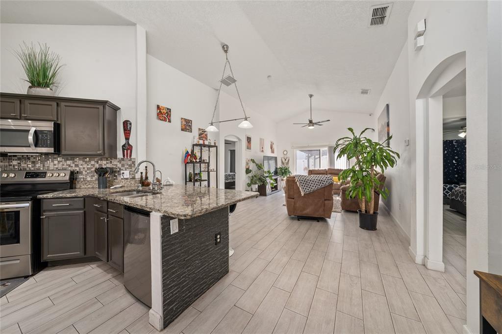 An open-concept kitchen with dark cabinets and granite countertops overlooks a living room area — 2822 MOULTRIE CREEK DRIVE, KISSIMMEE, FL