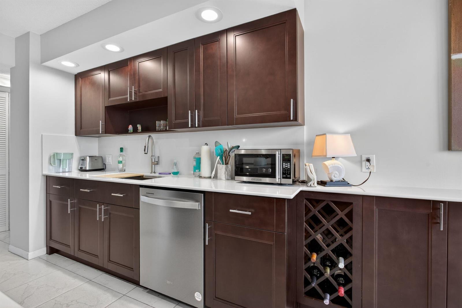 A kitchen features dark wood cabinets, white countertops, stainless steel appliances, and a wine rack — 1500 N Ocean Boulevard # 602, Pompano Beach FL 33062, POMPANO BEACH, FL