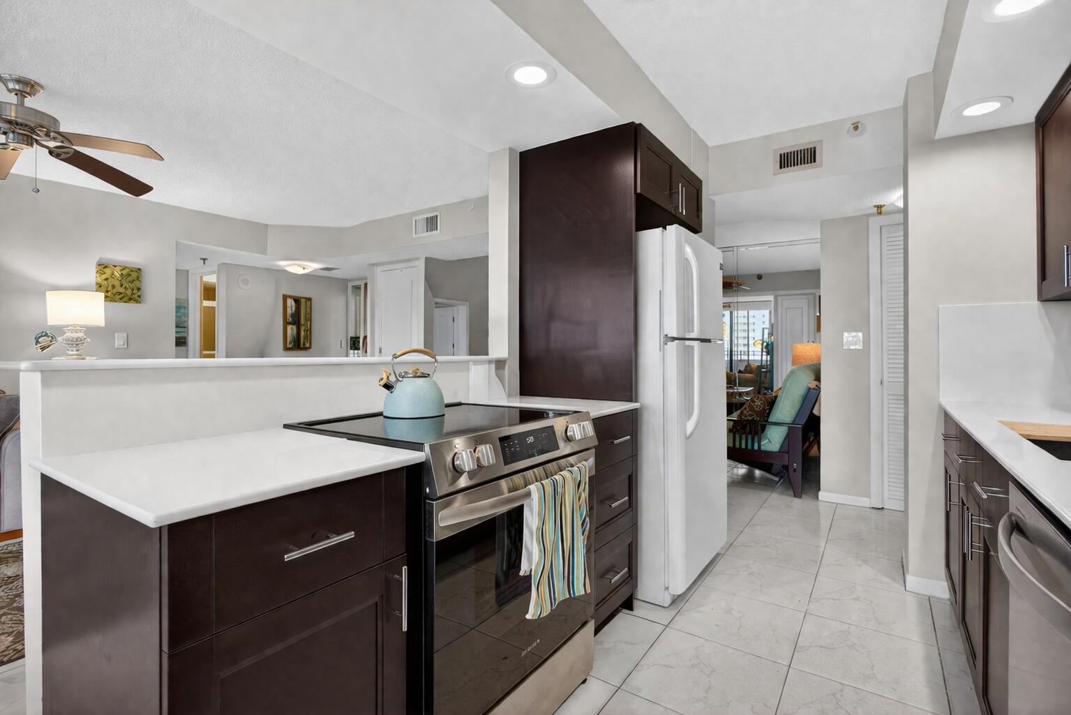 A kitchen features dark wood cabinets, white countertops, stainless steel appliances, and light tile flooring — 1500 N Ocean Boulevard # 602, Pompano Beach FL 33062, POMPANO BEACH, FL