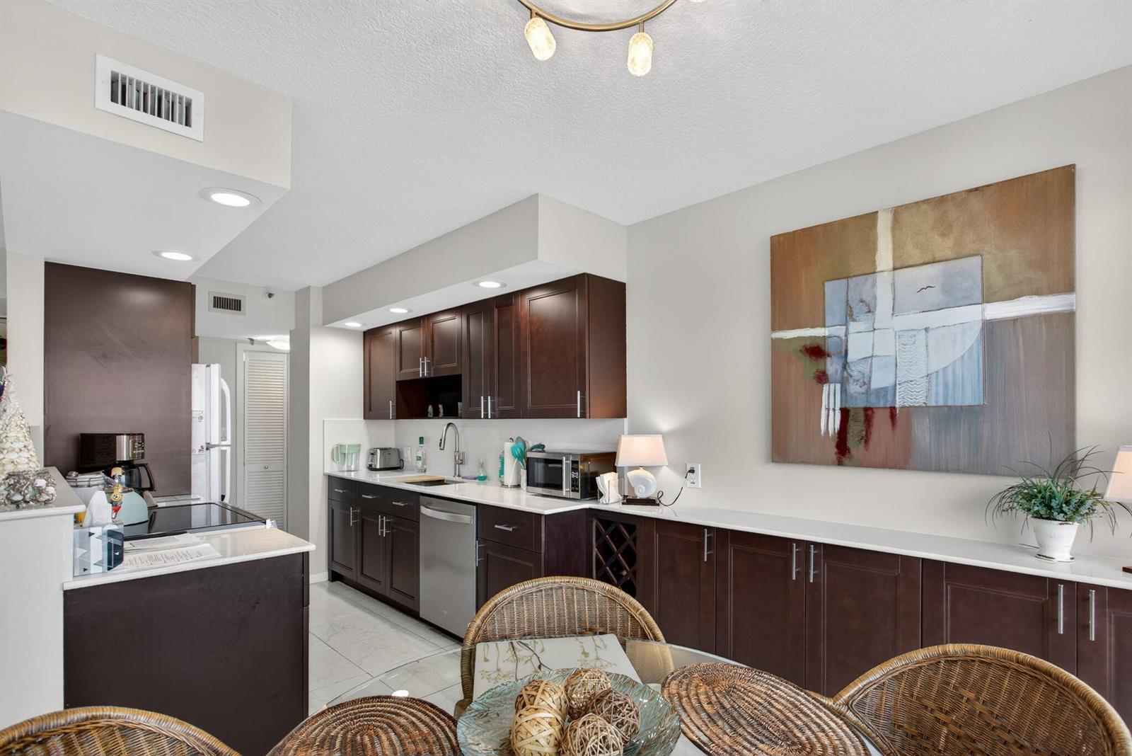 A kitchen features dark wood cabinets, white countertops, and a dining area with wicker chairs — 1500 N Ocean Boulevard # 602, Pompano Beach FL 33062, POMPANO BEACH, FL