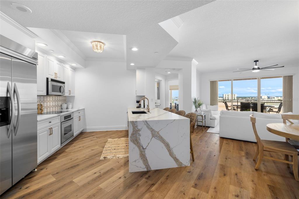 A modern kitchen with white cabinetry and a marble-topped island opens to a living area — 11 BAYMONT STREET UNIT 909, CLEARWATER BEACH, FL