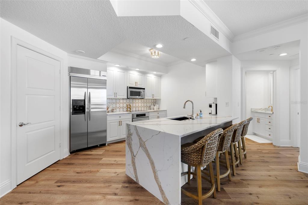 A modern kitchen features white cabinetry, a marble-topped island with bar seating, and wood flooring — 11 BAYMONT STREET UNIT 909, CLEARWATER BEACH, FL