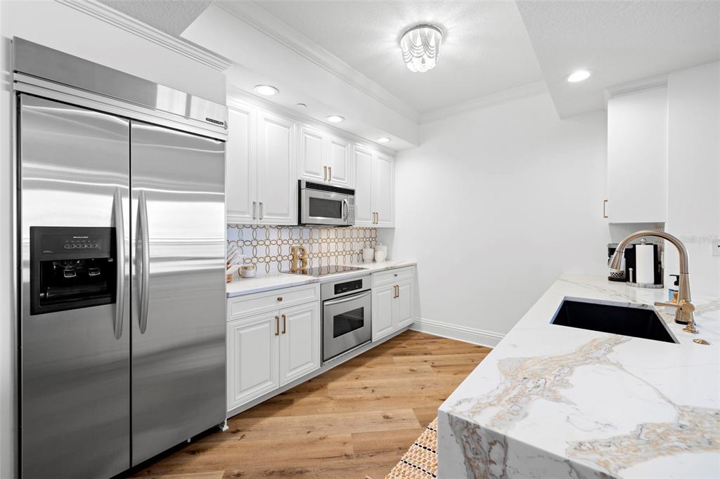 A modern kitchen features white cabinetry, stainless steel appliances, and a marble-topped island — 11 BAYMONT STREET UNIT 909, CLEARWATER BEACH, FL