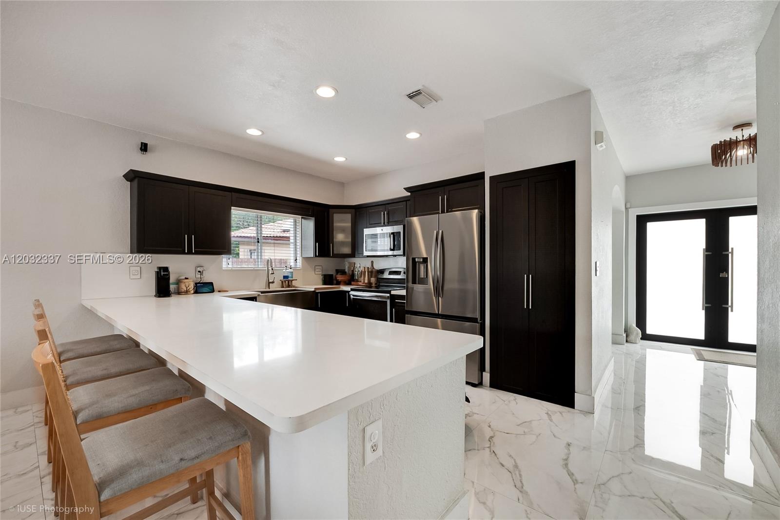 A modern kitchen features dark cabinetry, white countertops, stainless steel appliances, and marble-look flooring — 4147 NE 30th St, Homestead FL 33033, HOMESTEAD, FL